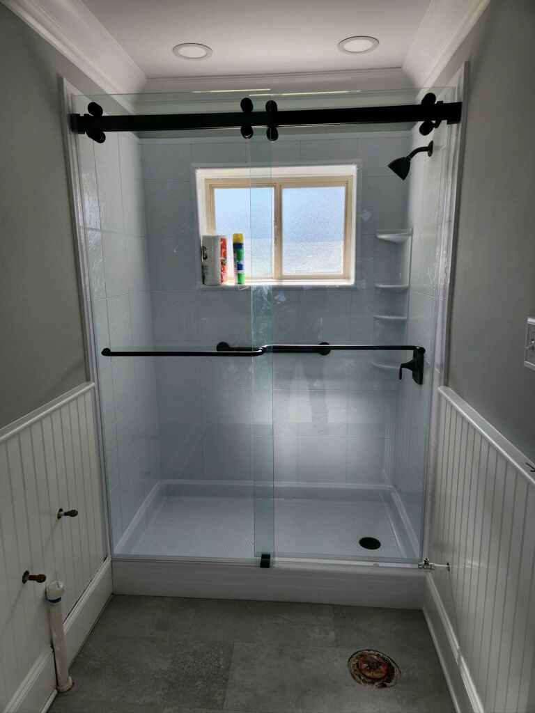 Walk-in shower with gray tile walls, white wainscoting, black grab bars, and a small window.