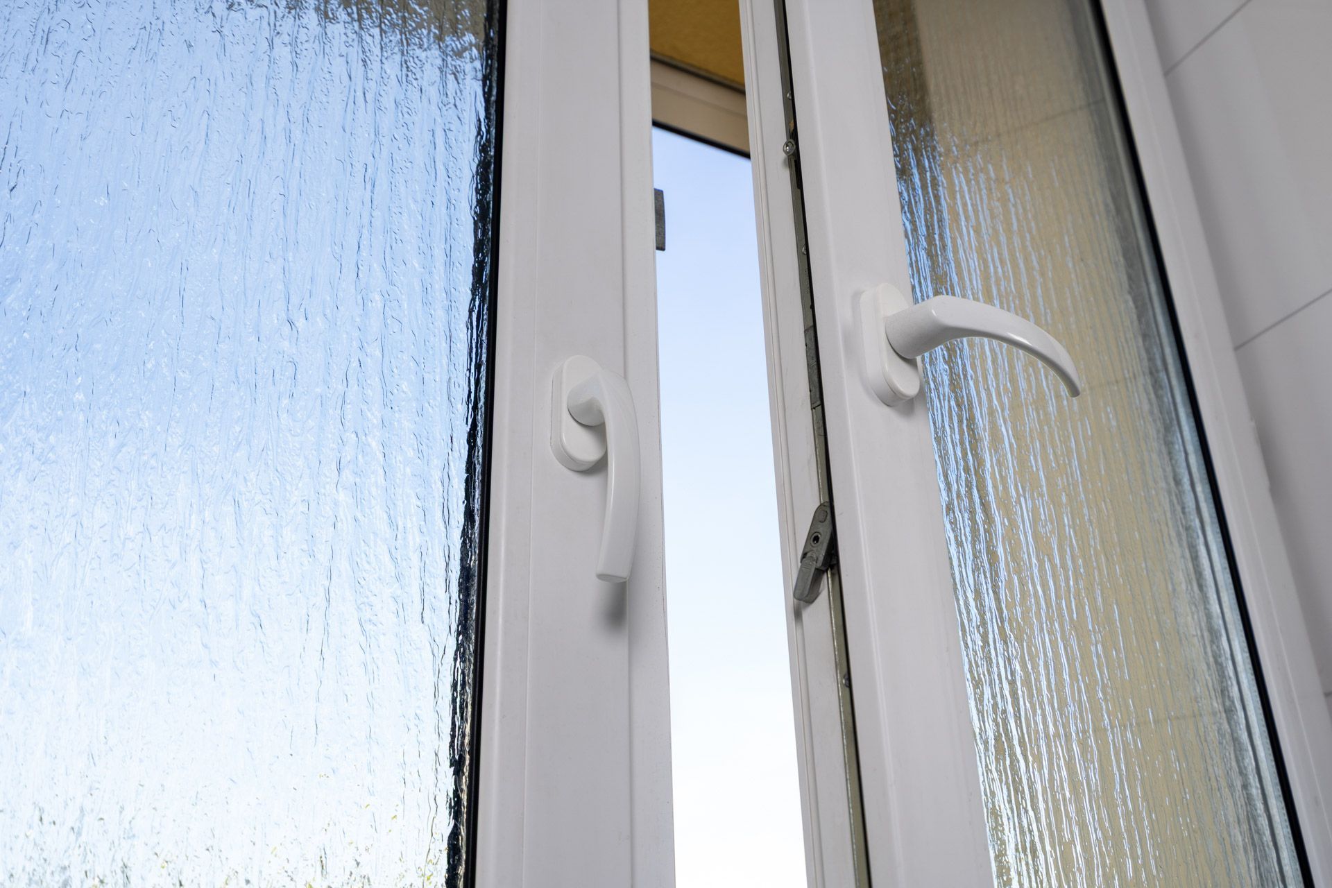 White window frame with two frosted glass panes and open handles, viewed from inside.