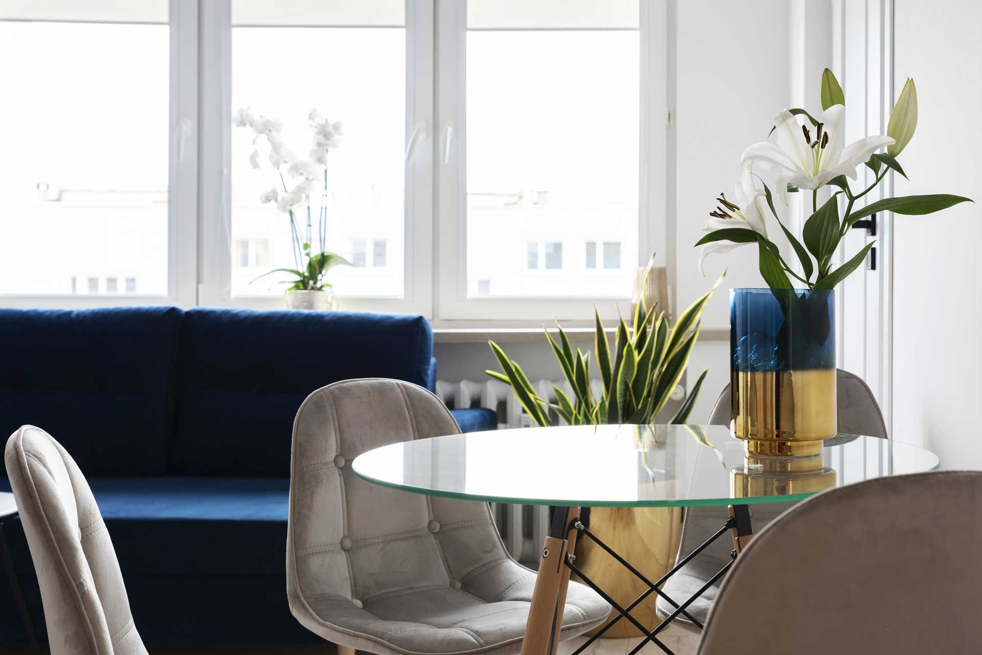 Bright living room with navy sofa, glass table, and white lilies by the window