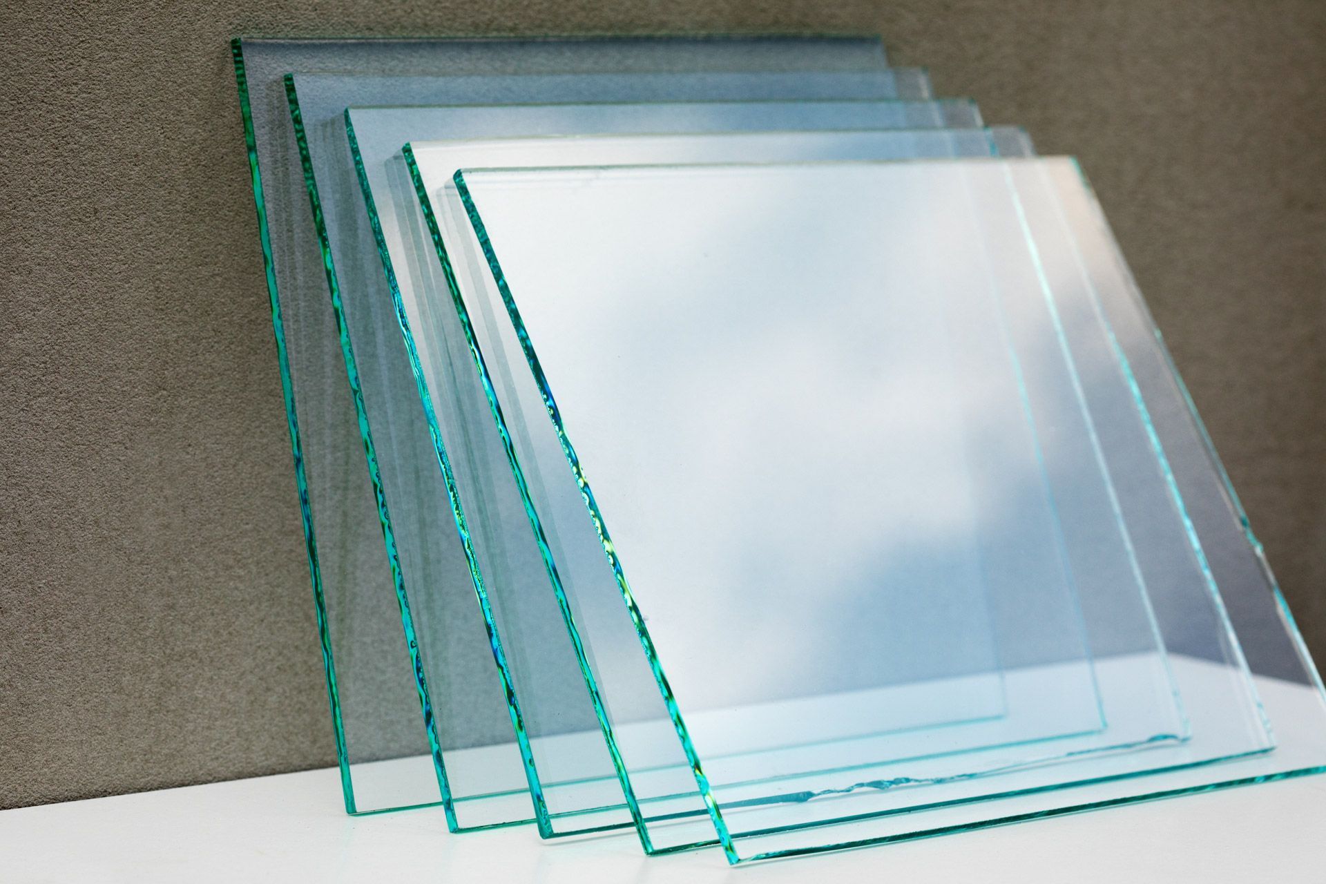 Stacked transparent glass panes leaning against a wall on a white surface.