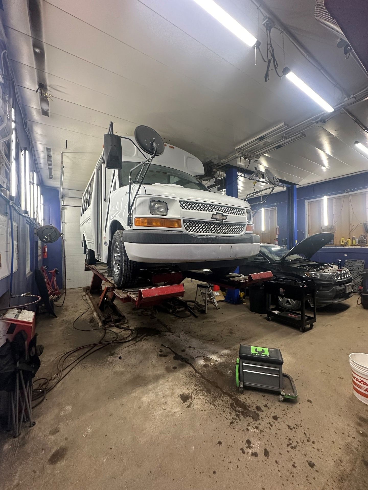 White SUV lifted in an auto repair shop, with tools and equipment around it.