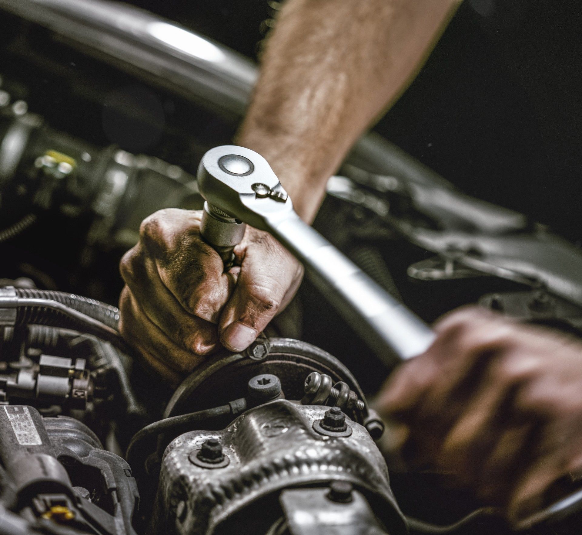 Hands using a ratchet wrench to repair a car engine in a dim garage
