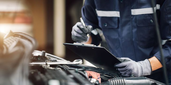 Mechanic in dark uniform inspecting a car engine with a wrench in a garage