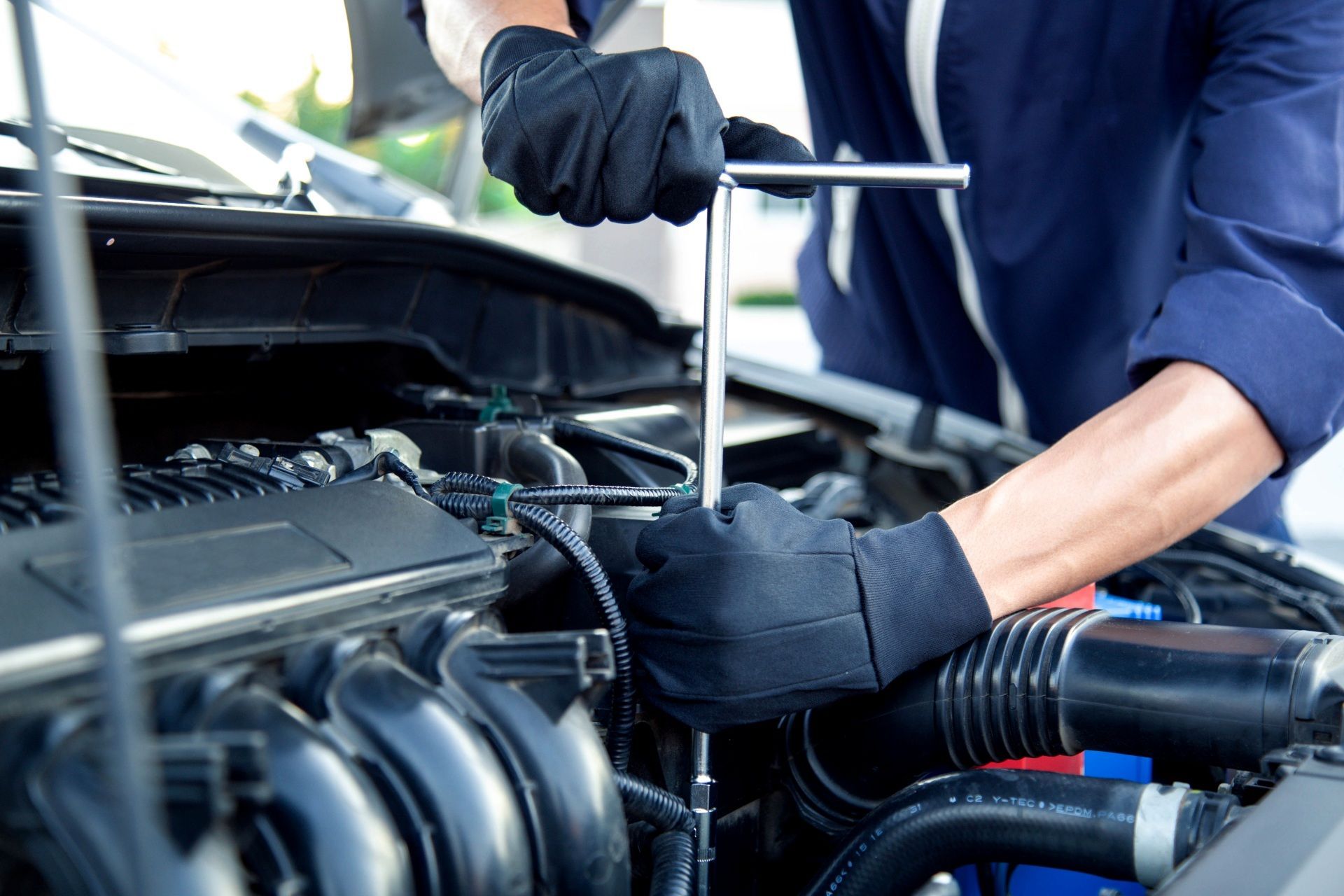 Mechanic wearing gloves working under a car hood with a wrench in an engine bay