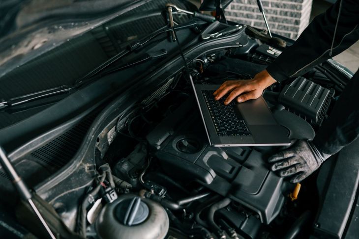 Mechanic using a laptop in a car engine bay to diagnose a vehicle problem