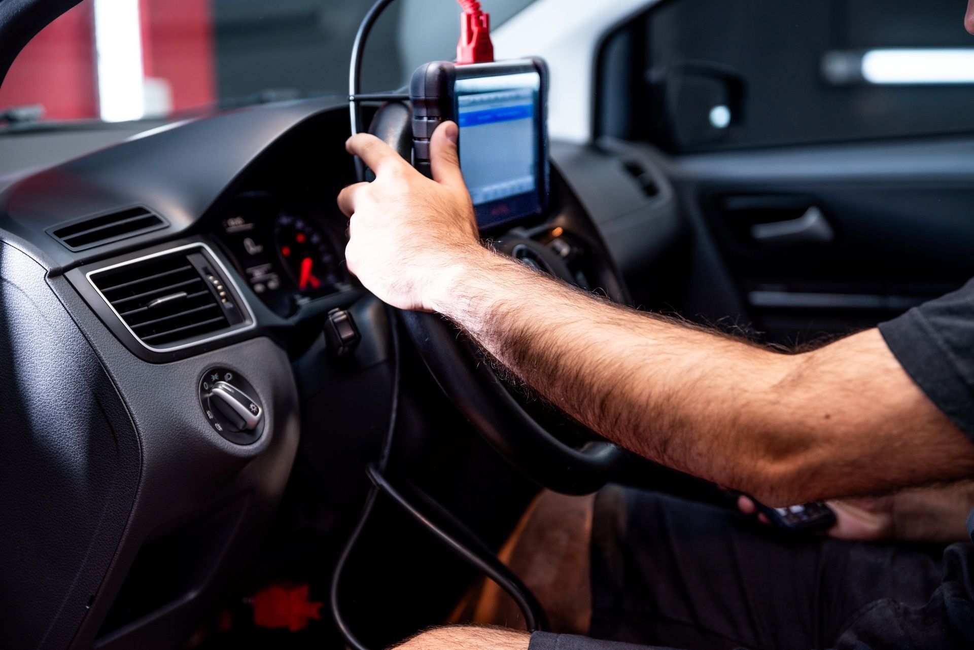 Mechanic using a diagnostic tool inside a car dashboard with a red cable attached