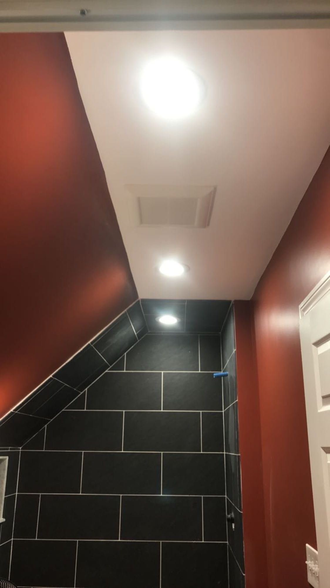 A room with red walls and black tiles and a ceiling fan.