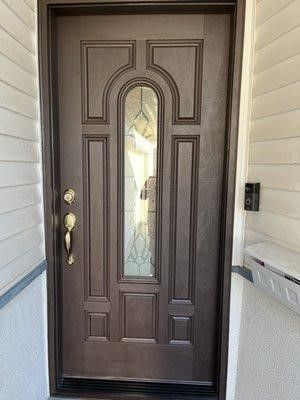 A brown front door with a glass window on a white house.