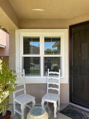 A porch with two chairs and a table in front of a window.