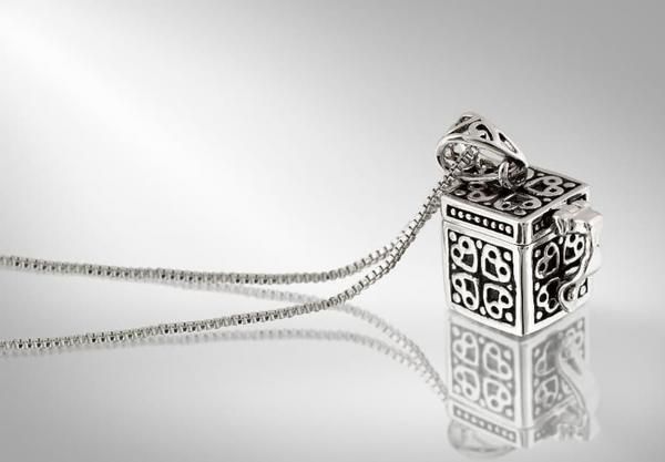 Ornate silver pendant necklace with black-and-white square design on a reflective white surface
