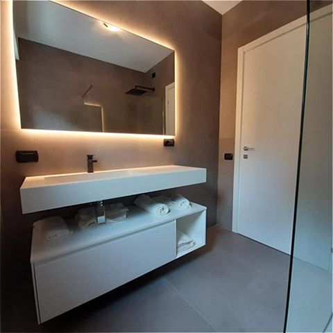Bagno moderno con lavabo sospeso, grande specchio retroilluminato, porta bianca e box doccia in vetro.