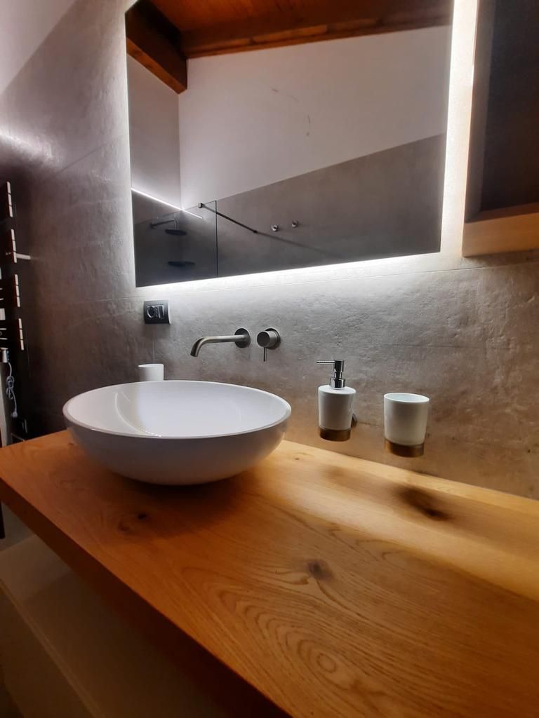 Mobile bagno moderno con lavabo rotondo bianco, piano in legno, specchio e dispenser di sapone.