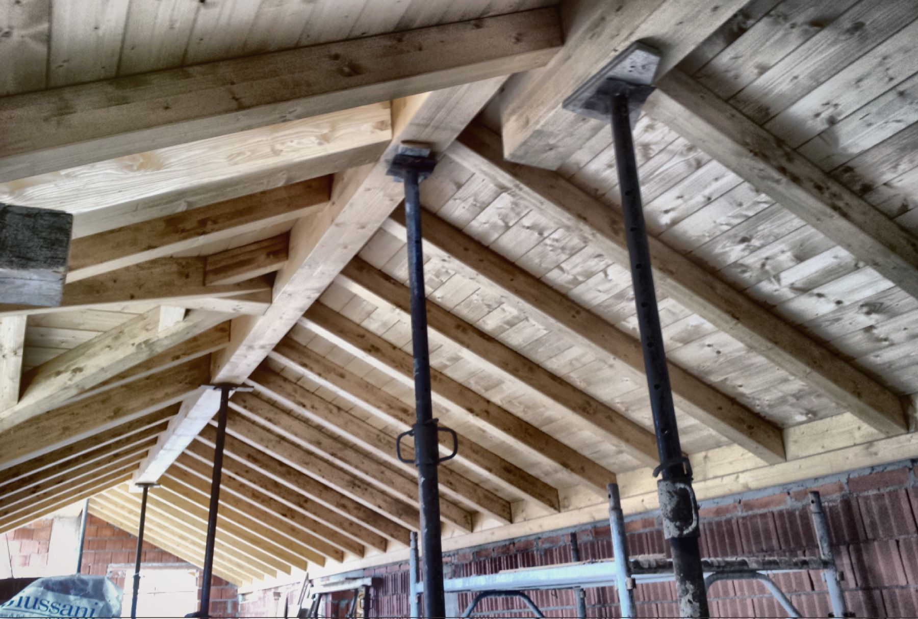 Travi di legno per il tetto in fase di costruzione con pali di sostegno neri in un edificio parzialmente terminato