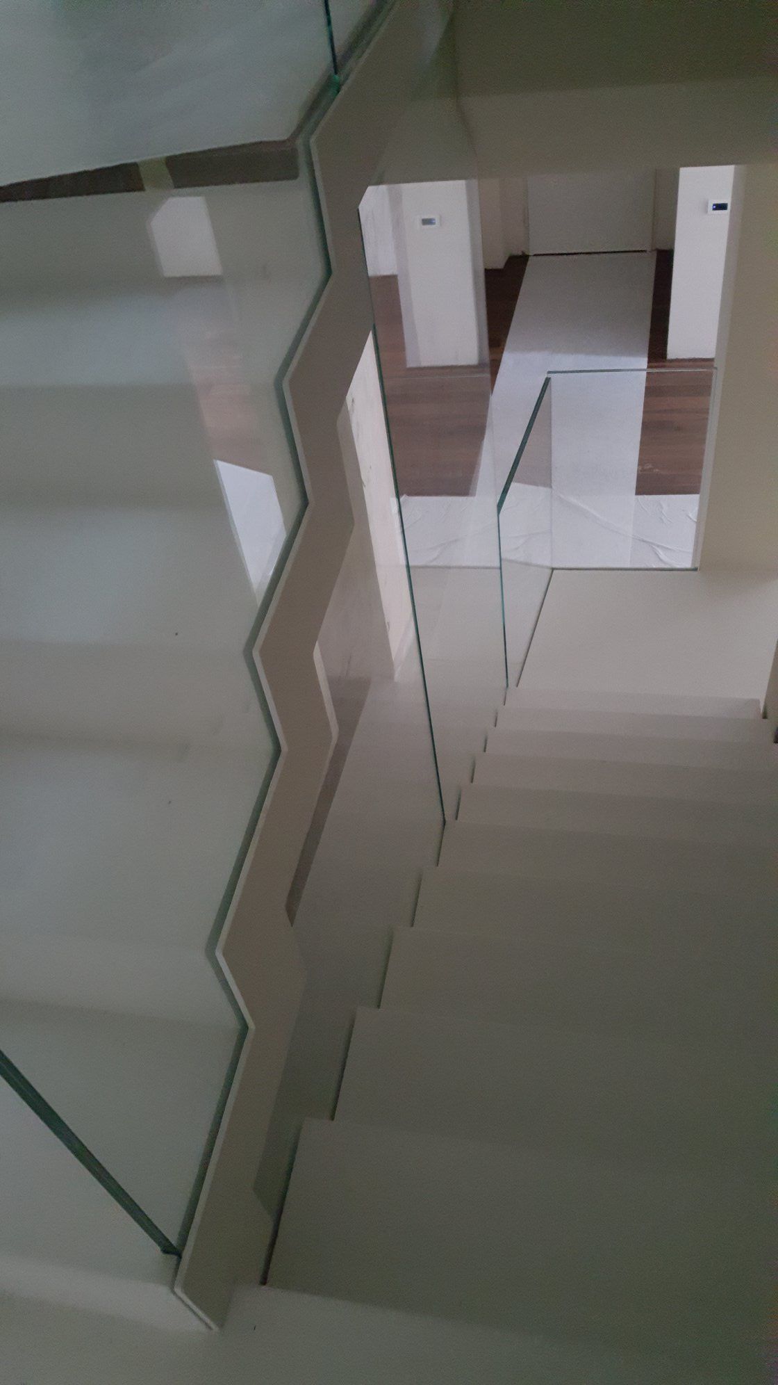 Scala piastrellata di bianco con ringhiera in vetro e montanti bianchi che conduce al piano inferiore.