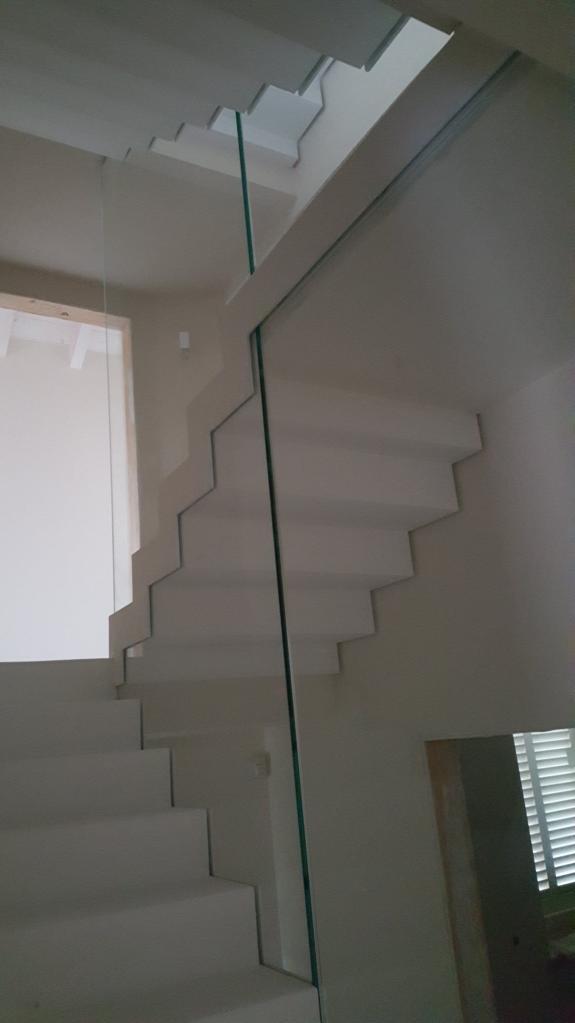 Scala interna con pareti bianche e ringhiera verticale in vetro che conduce al piano superiore.