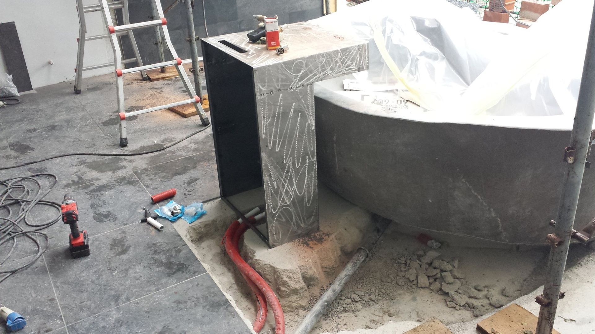 Cantiere edile con scala, utensili elettrici e una grande vasca rotonda in cemento in fase di ristrutturazione.