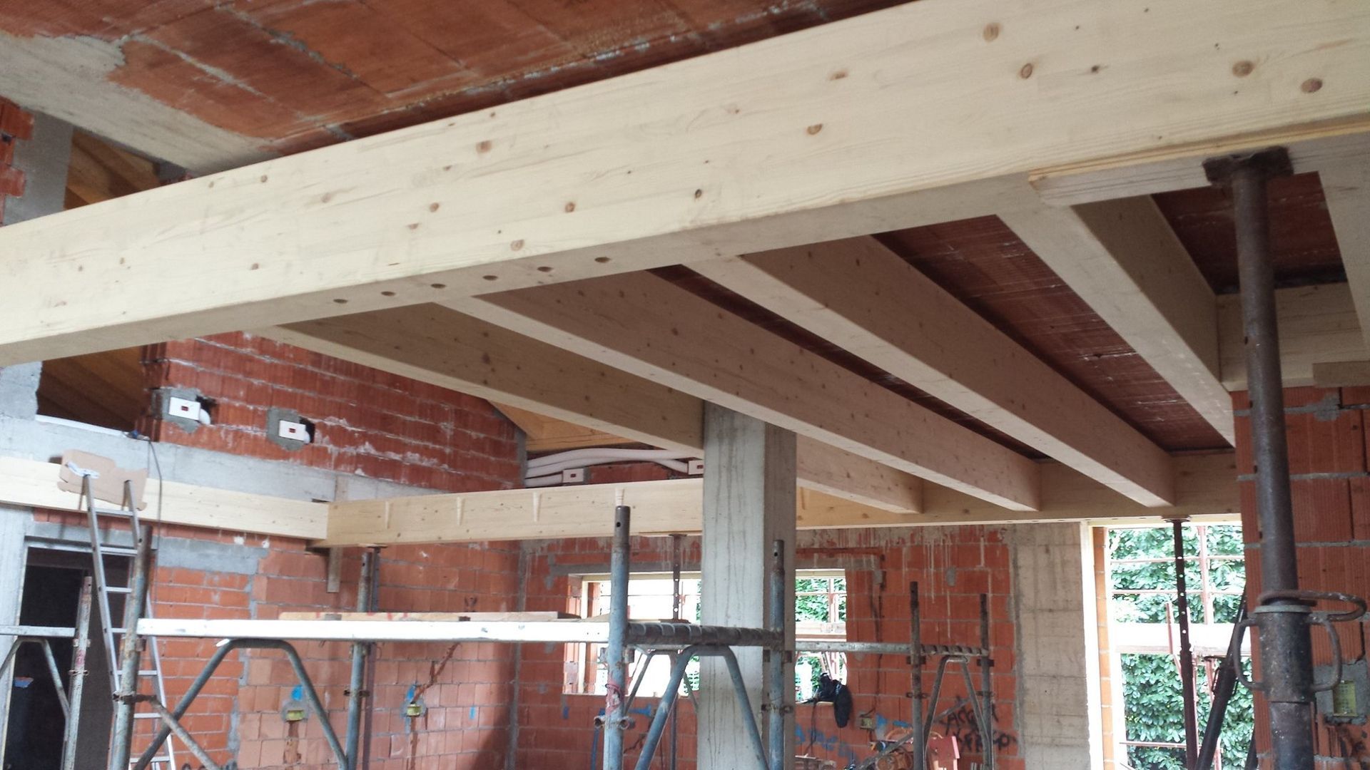 Interno di un cantiere edile con travi in legno a vista, impalcature e muri in mattoni in fase di ristrutturazione.