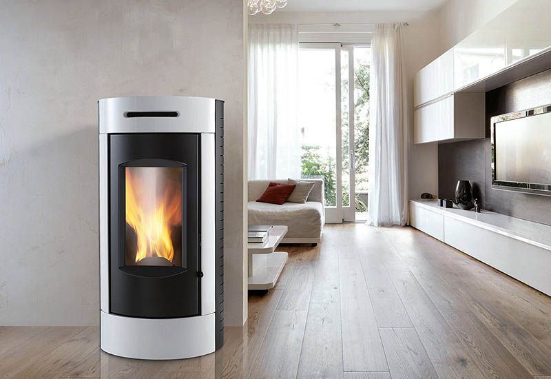 Soggiorno moderno con stufa a pellet color argento accesa vicino a una finestra luminosa e parete attrezzata con televisore.
