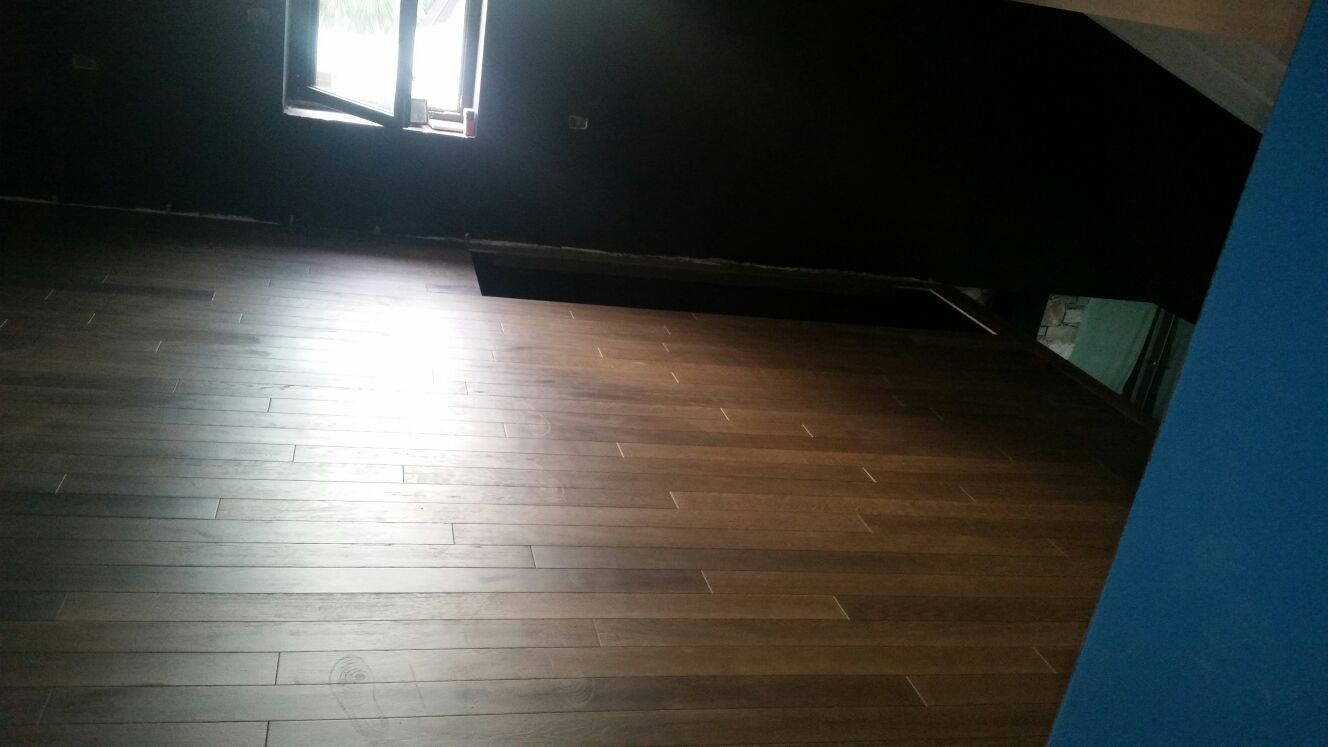 Pavimento in legno vuoto in una stanza buia, illuminato dalla luce del sole che entra da una finestra.