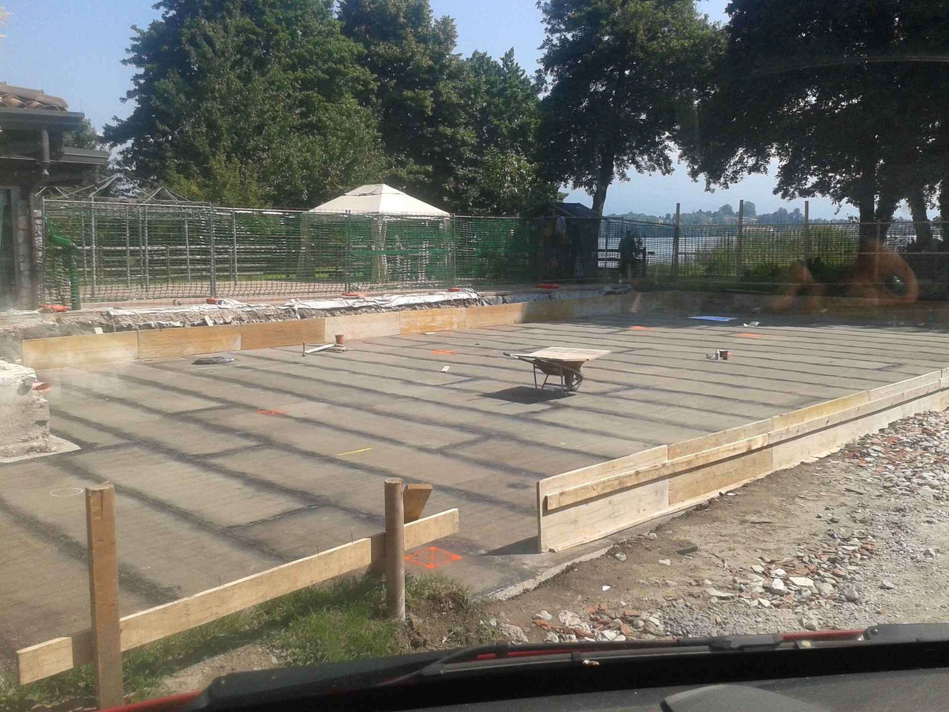 Fondazione in cemento parzialmente realizzata con casseforme in legno in un cortile esterno soleggiato.