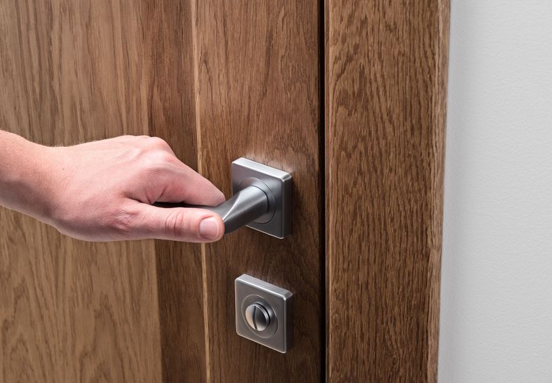 Mano che gira una maniglia d'argento su una porta di legno, con una serratura sottostante.
