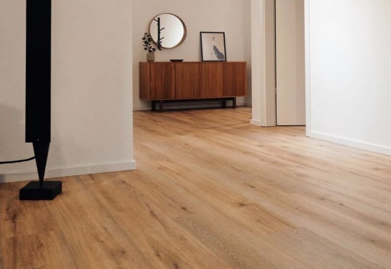 Corridoio minimalista con pavimento in legno chiaro, pareti bianche e una credenza in legno con elementi decorativi.