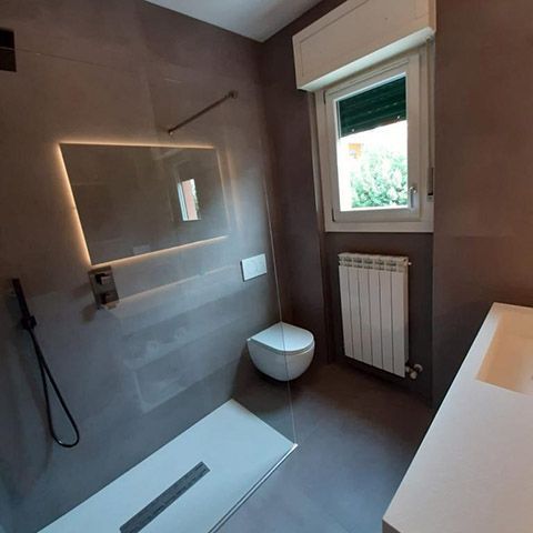 Bagno moderno con cabina doccia, lavabo a parete, WC e finestra sopra il termosifone.