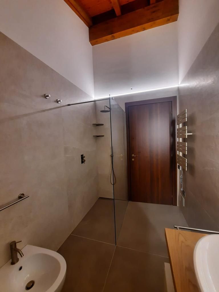 Bagno moderno con cabina doccia, pareti piastrellate di bianco, soffitto in legno e porta in legno.