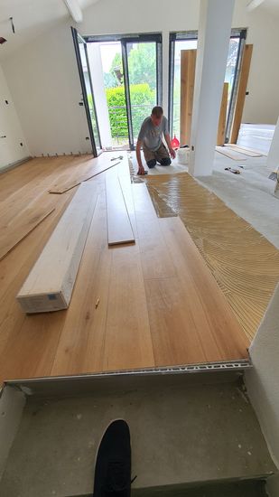 Stretto corridoio con pavimento in legno a spina di pesce, pareti bianche e lucernario sul soffitto.