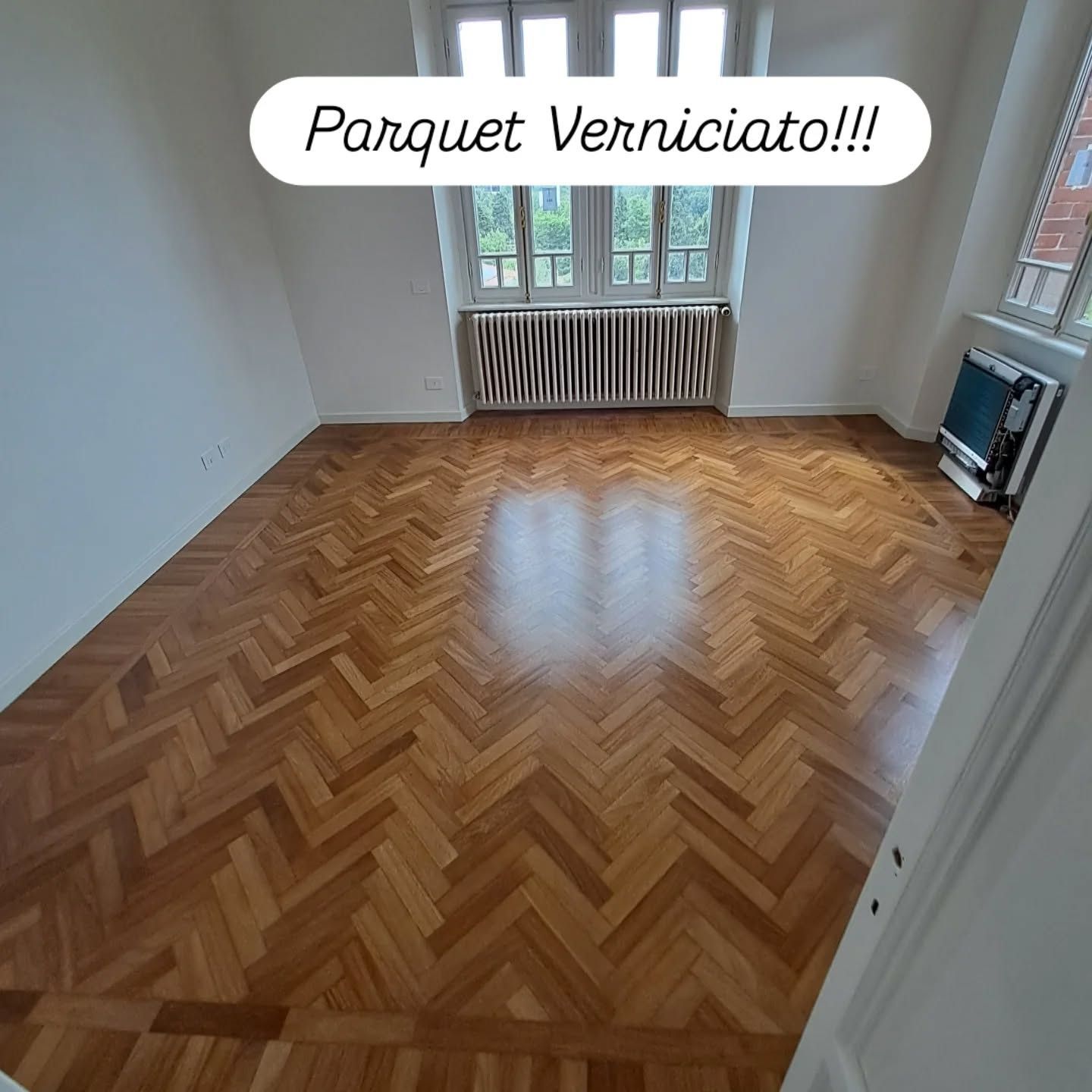 Pavimento in parquet a spina di pesce lucidato in una stanza luminosa e vuota con finestra e termosifone.