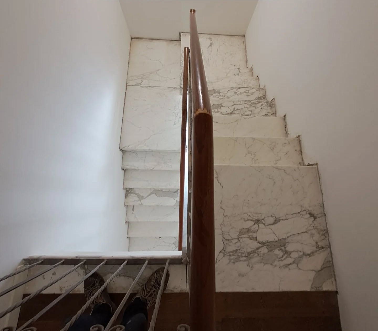 Scala in marmo con corrimano in legno e pareti bianche, vista dai gradini inferiori.