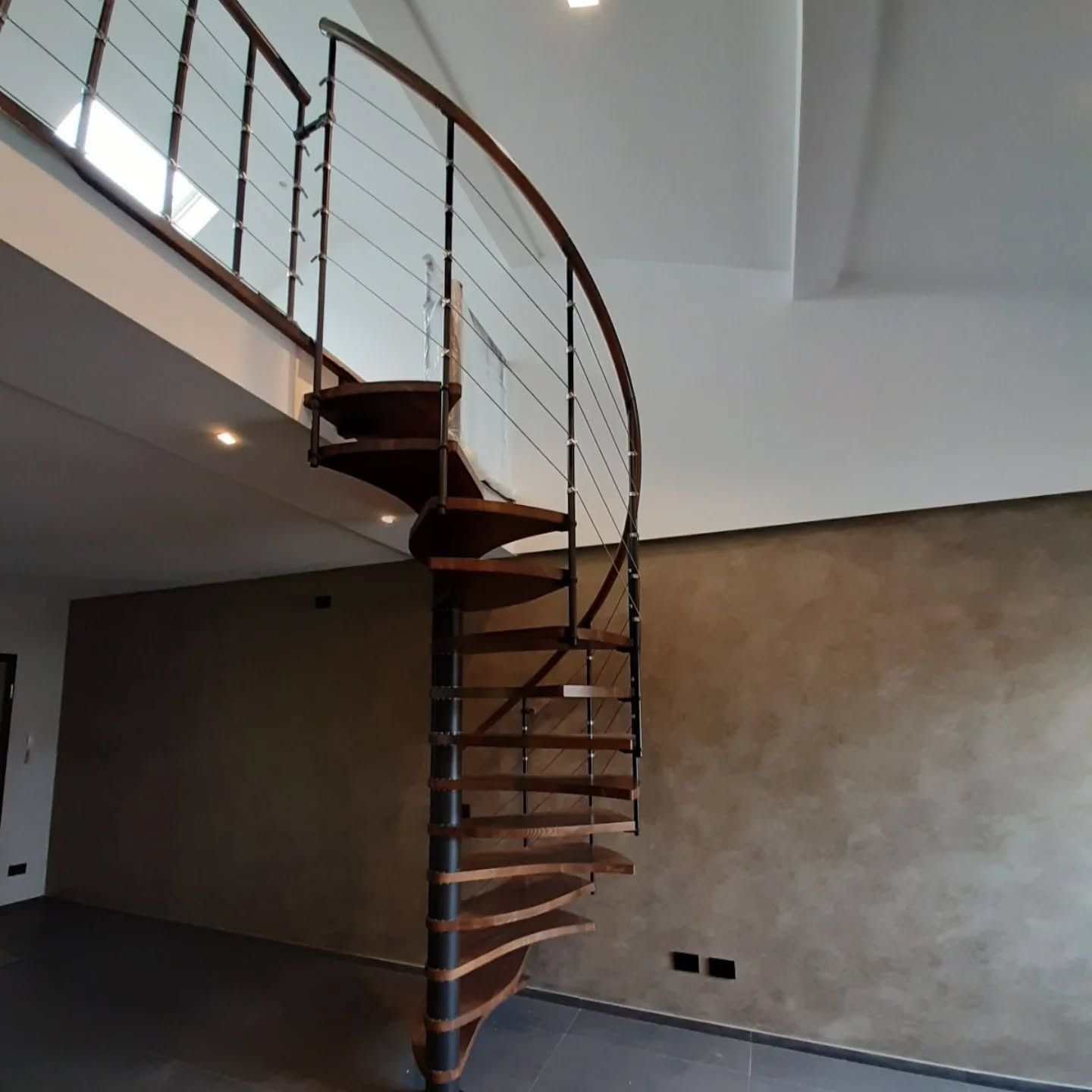 Interno moderno con scala a chiocciola in legno curva e ringhiera in metallo accanto a una parete beige.