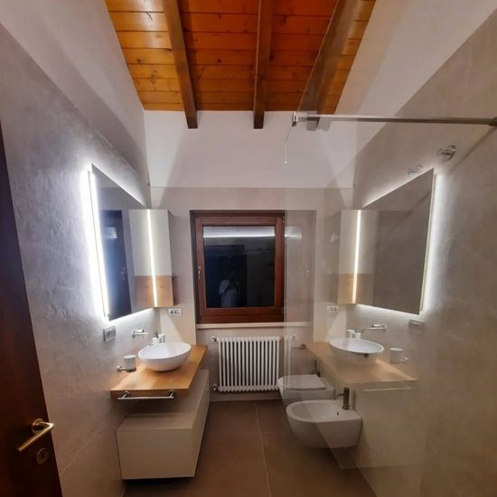 Bagno stretto con doppio lavabo, specchi a parete, una finestra e soffitto con travi in legno.
