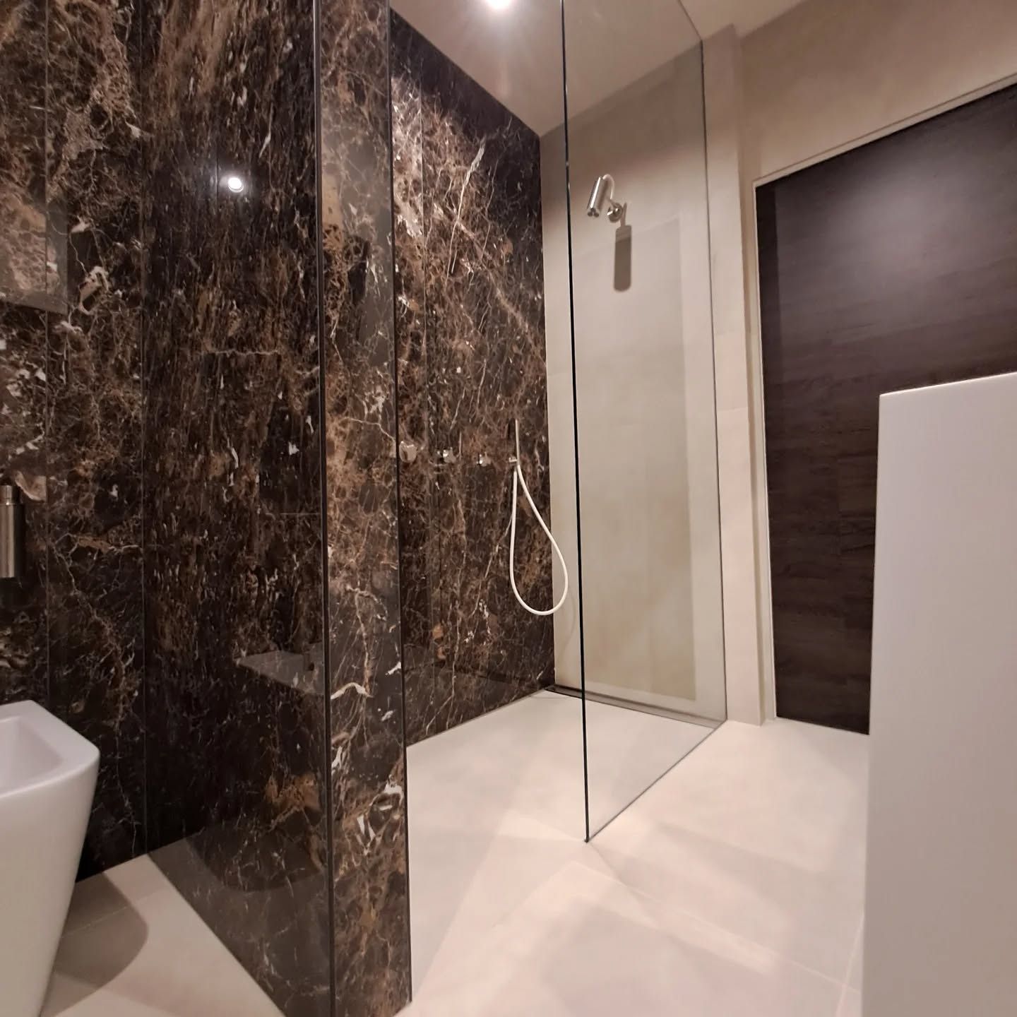 Bagno moderno con pareti in marmo, box doccia in vetro e pavimento bianco.
