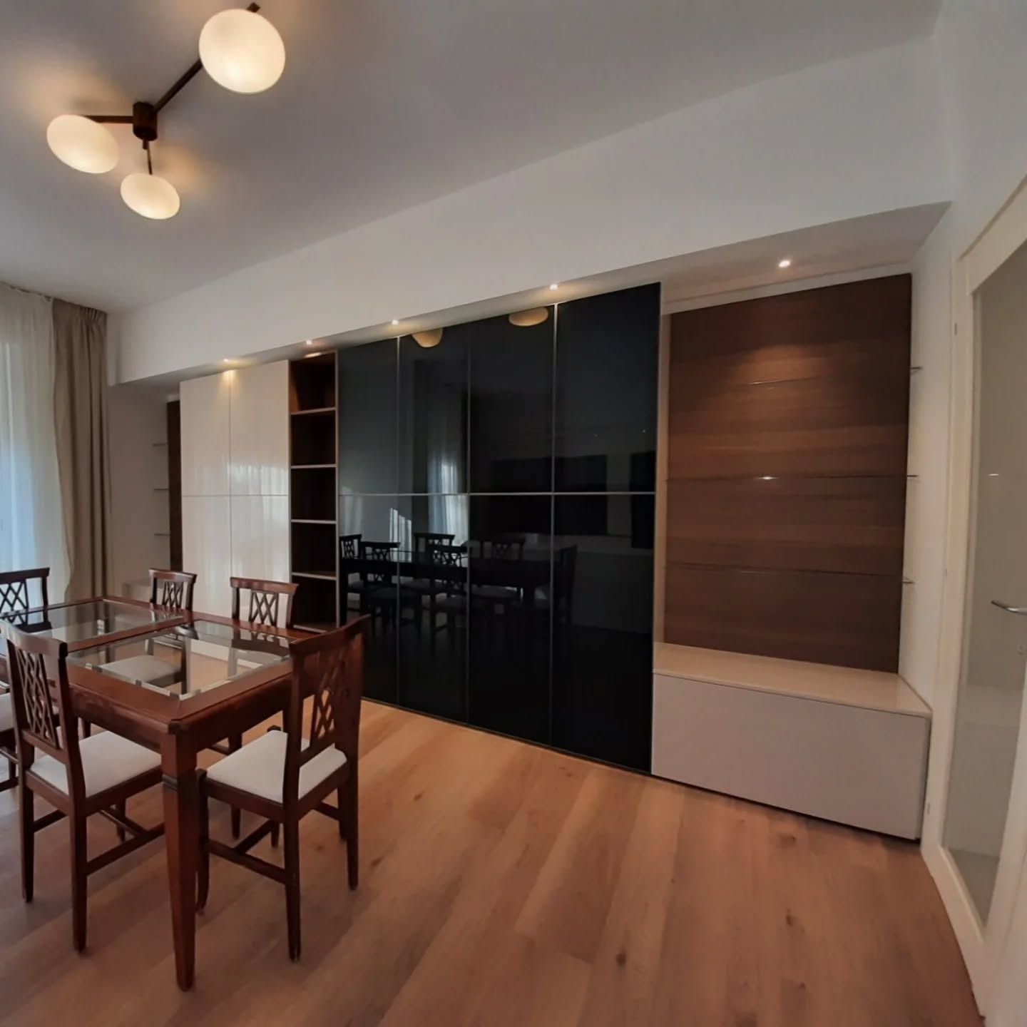 Sala da pranzo moderna con tavolo e sedie in legno, mobile a muro nero lucido e vani contenitori a parete rivestiti in legno.