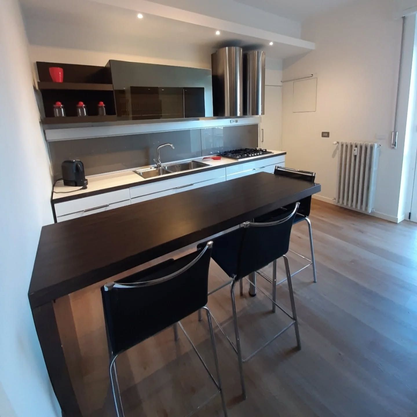Cucina moderna con isola e bancone per la colazione, sedie nere ed elettrodomestici in acciaio inossidabile.