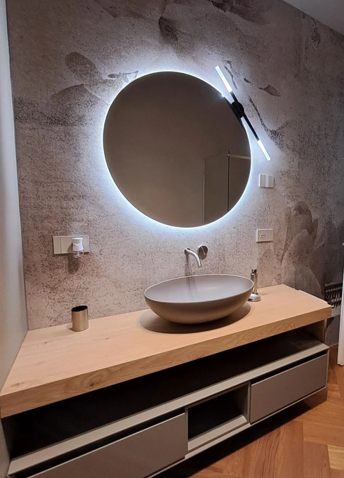 Mobile bagno moderno con specchio rotondo retroilluminato, lavabo in pietra e piano d'appoggio sospeso in legno.