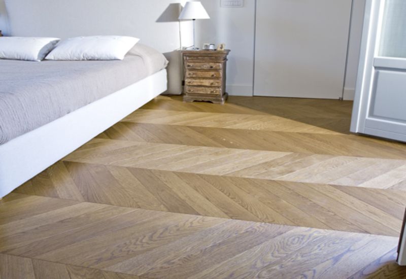 Camera da letto con letto, comodino e pavimento in parquet a spina di pesce in tonalità di legno chiaro.