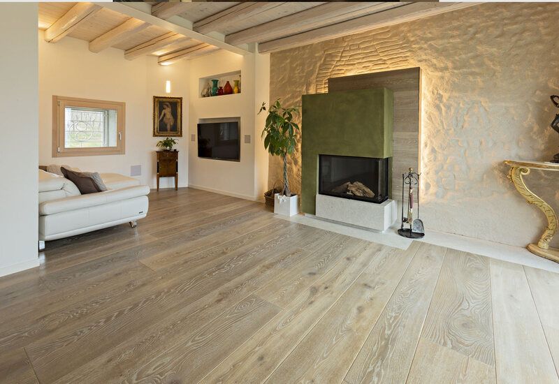 Luminoso soggiorno moderno con divano bianco, camino in pietra e pavimento in legno chiaro.
