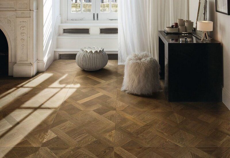 Stanza luminosa con pavimento in legno a spina di pesce, tende trasparenti e moderni sgabelli decorativi accanto a una consolle nera.