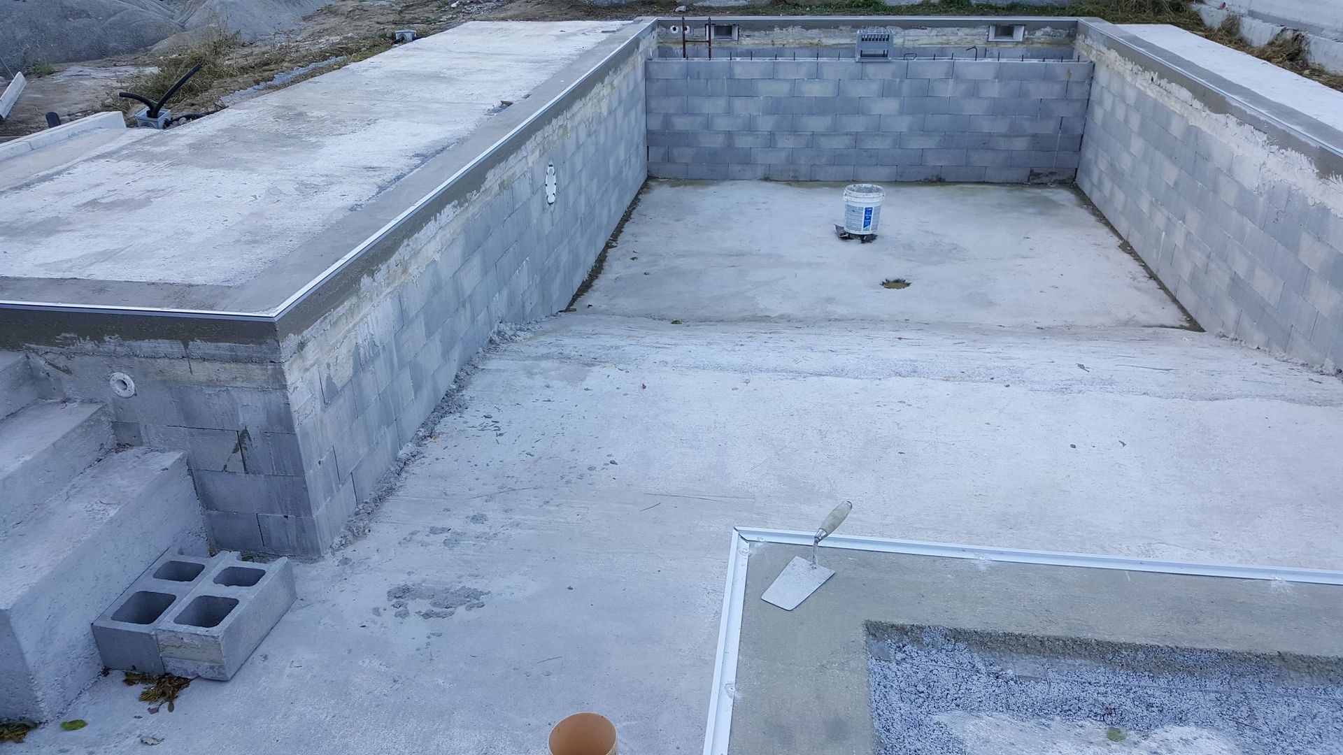 Piscina sul tetto vuota, in fase di ristrutturazione, con pareti in cemento e pavimento bianco.