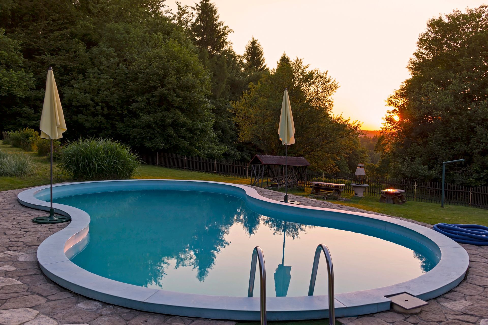 Tranquilla piscina nel cortile sul retro al tramonto, con acqua azzurra, lettini e alberi che circondano la terrazza.