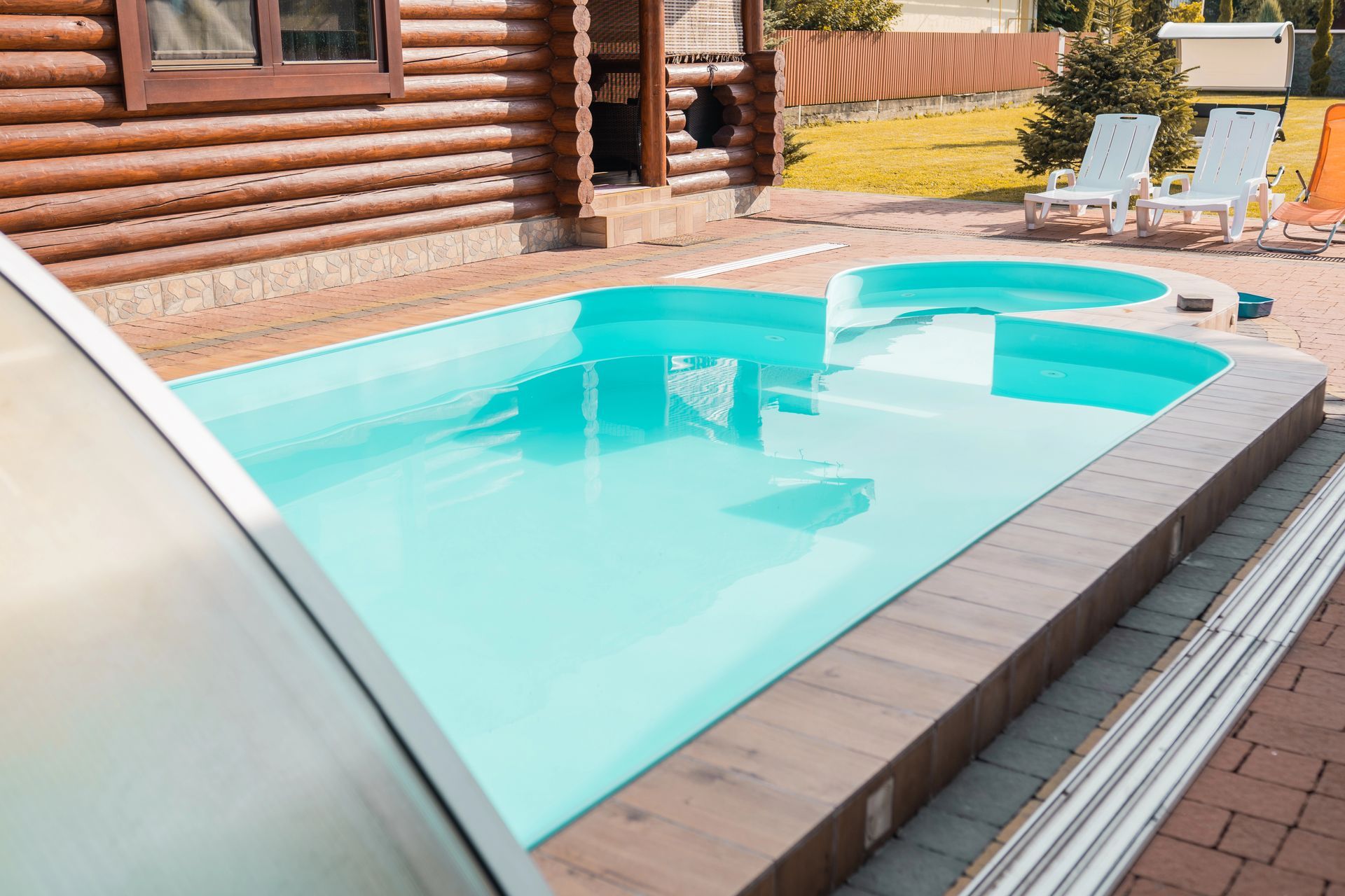 Piscina nel cortile sul retro, accanto a una baita in legno, con sedie a sdraio e terrazza pavimentata.