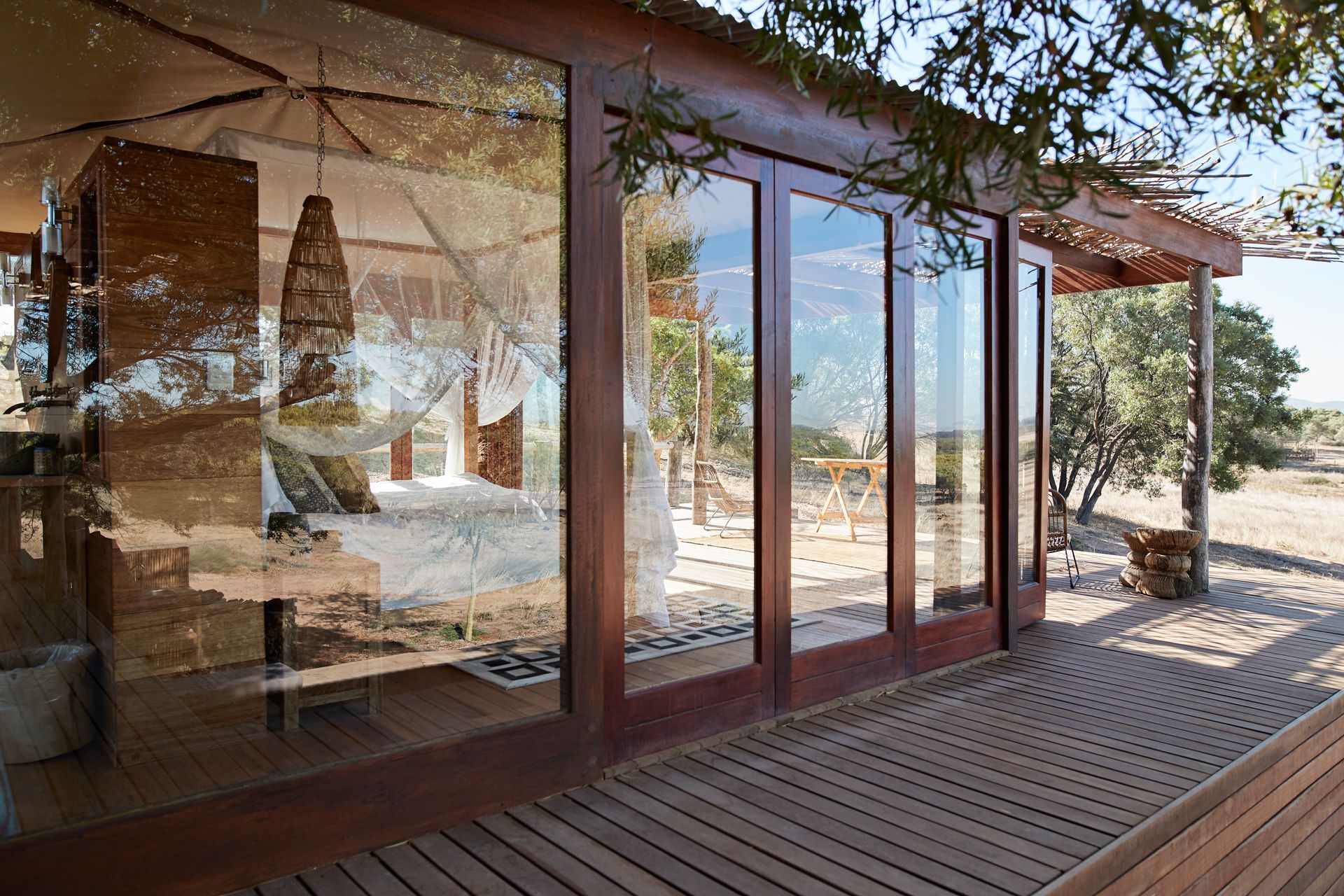 Terrazza in legno con porte scorrevoli in vetro che riflettono un patio soleggiato e il paesaggio circostante.