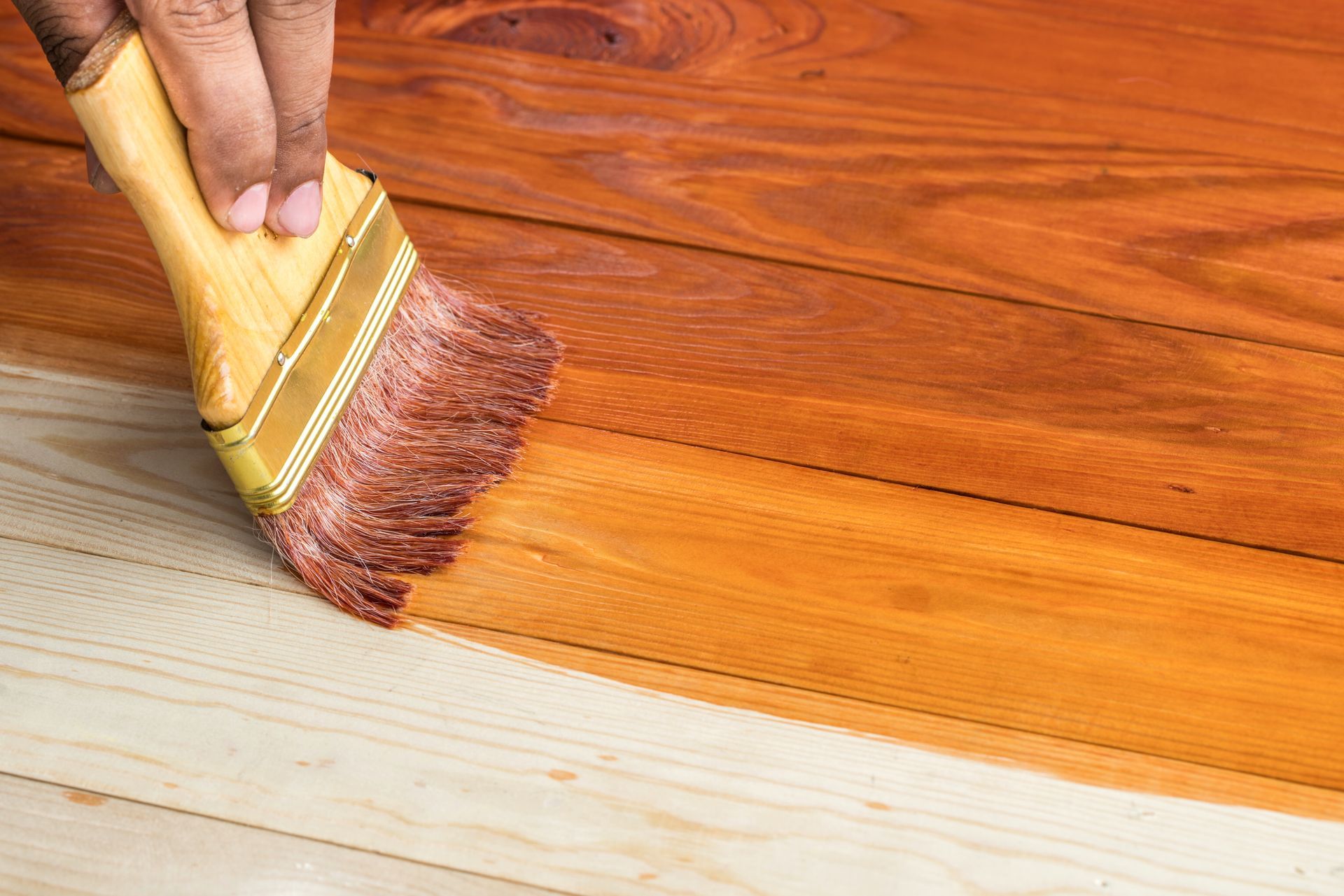 Applicare con un pennello una tinta marrone su una superficie di legno, lasciando una ricca finitura ambrata accanto al legno grezzo.