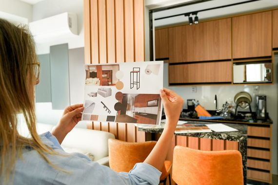 Persona che tiene in mano una rivista in una cucina moderna con mobili in legno e sgabelli arancioni.