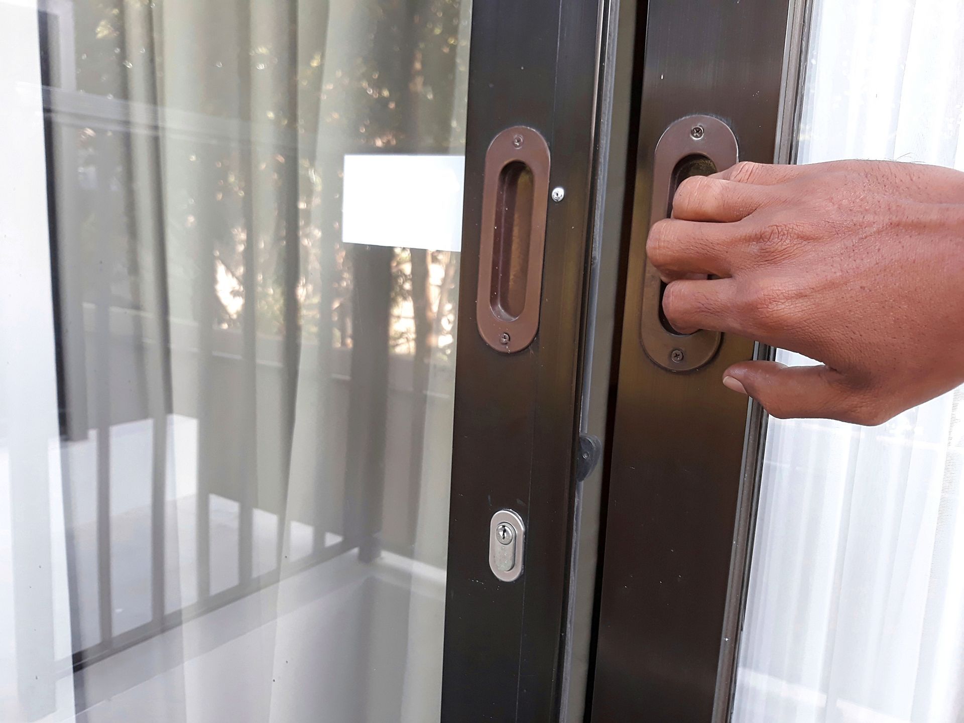 Una mano apre una porta marrone dall'esterno attraverso una stretta fessura per la maniglia.