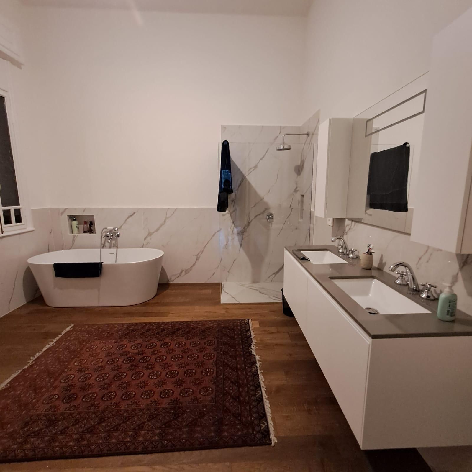 Bagno moderno con vasca freestanding, doppio lavabo, tappeto rosso e pavimento in legno.