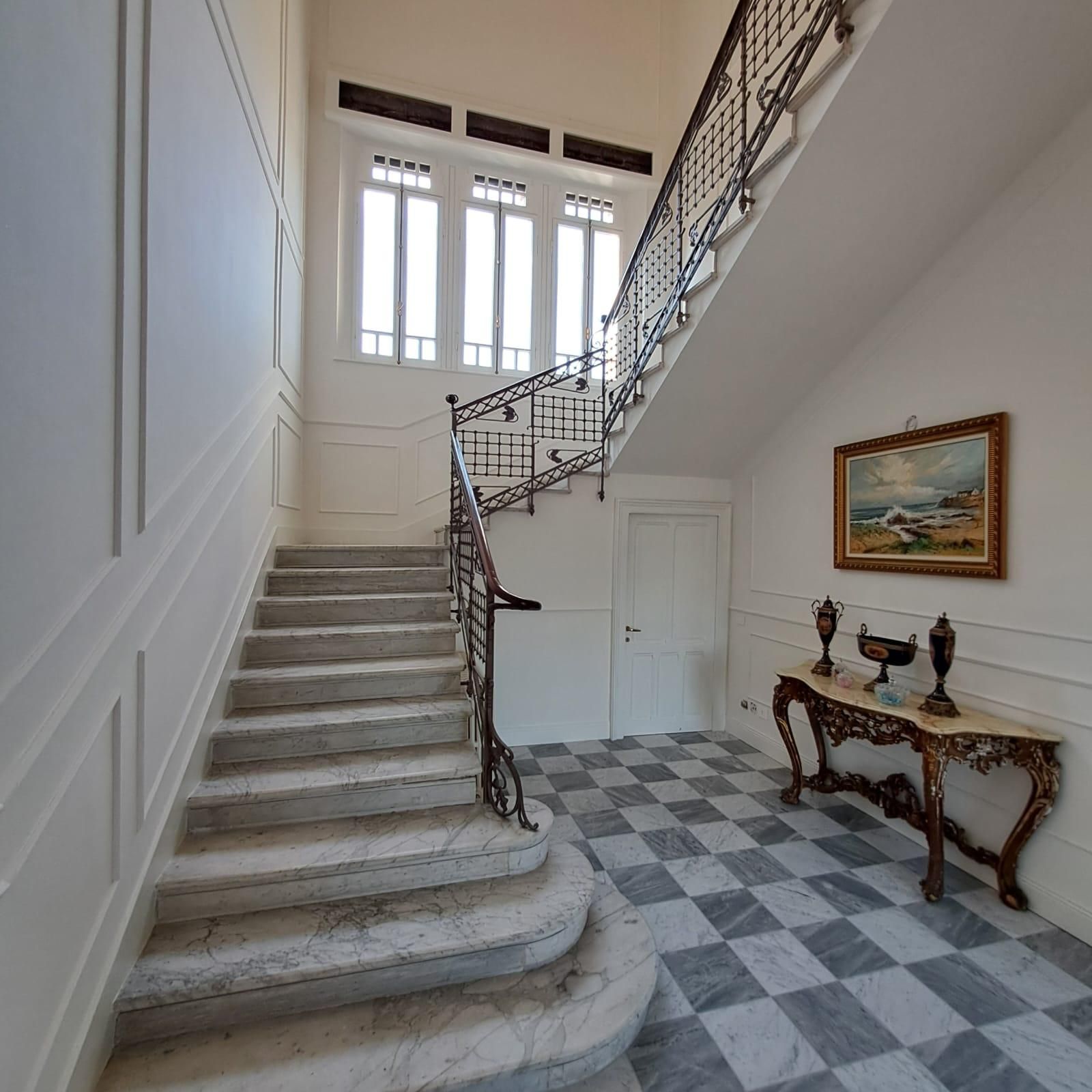 Elegante atrio con scalinata in marmo, pavimento a scacchiera e consolle decorata sotto un dipinto.