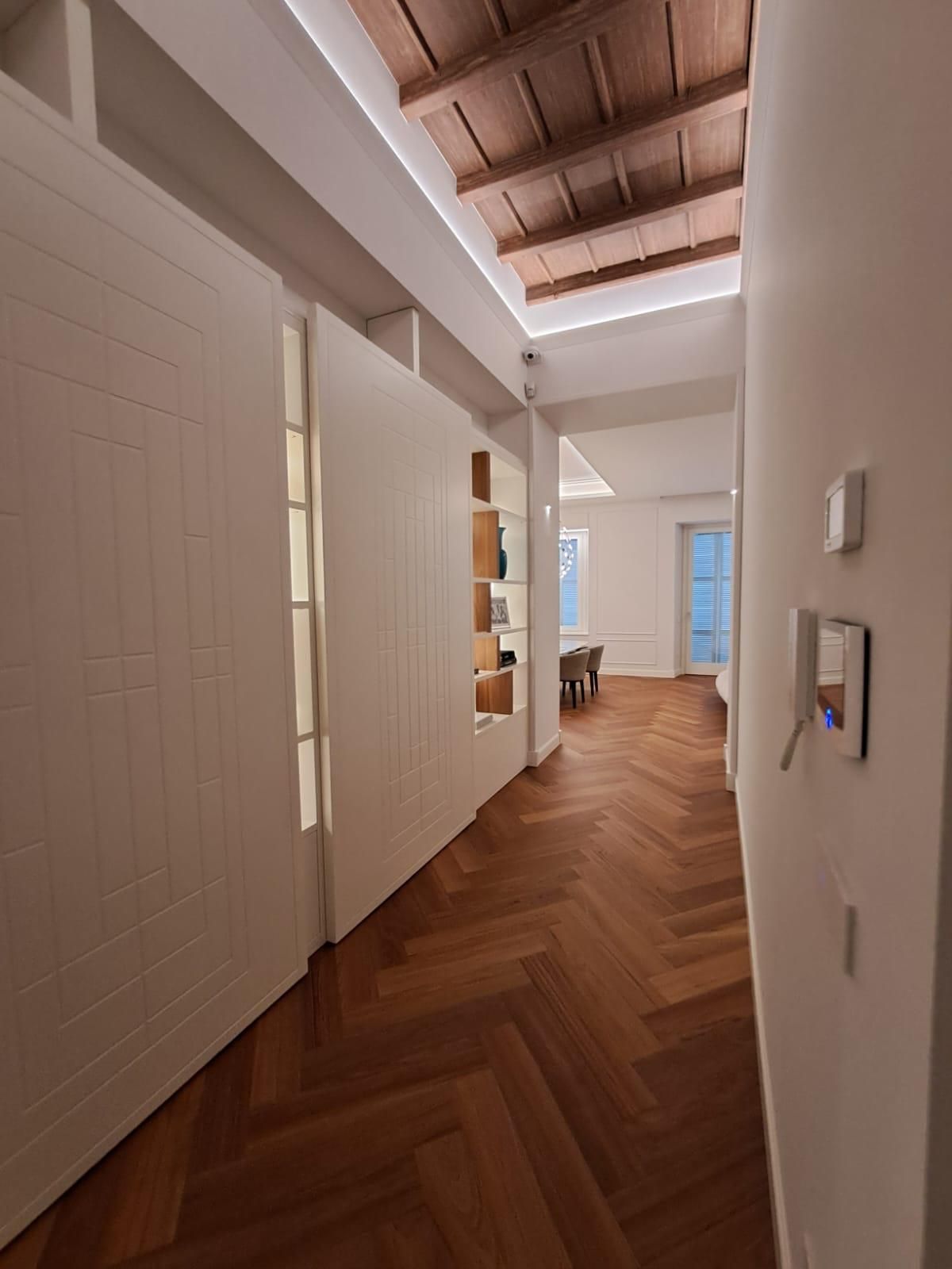 Stretto corridoio con pavimento in legno a spina di pesce, pareti bianche e lucernario sul soffitto.